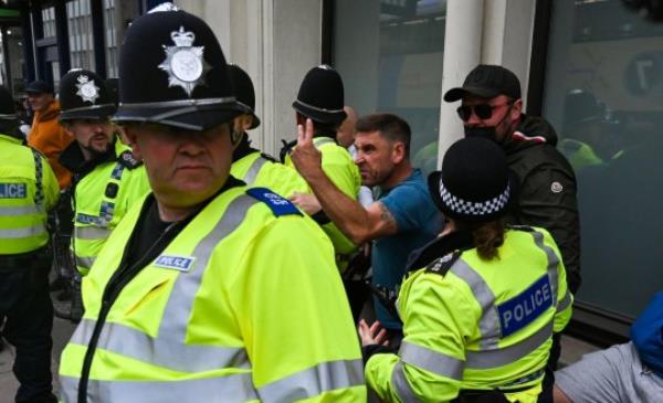 A scowling man lifts his finger at anti-fascists as he's surrounded by police.